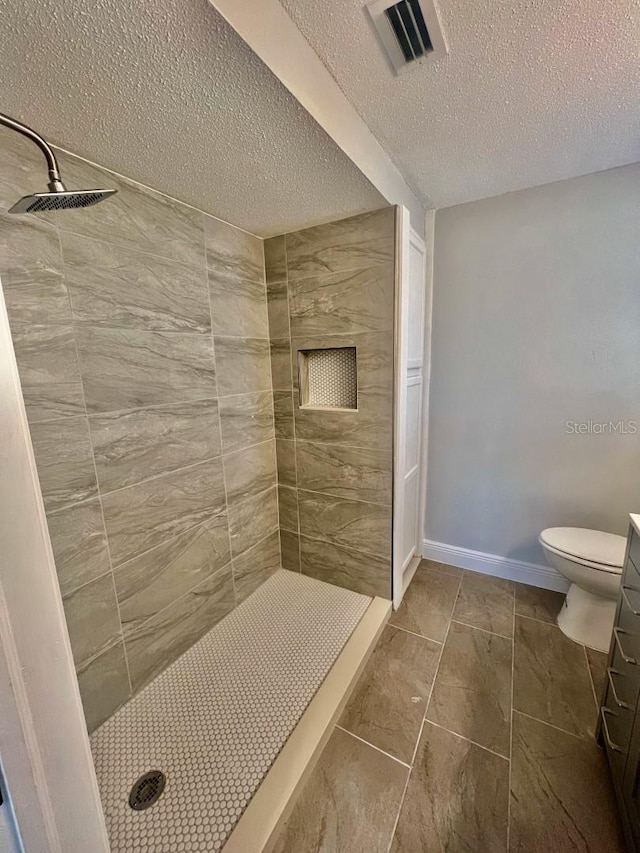 bathroom with vanity, tile patterned flooring, toilet, a textured ceiling, and a tile shower