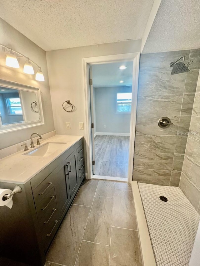 bathroom with plenty of natural light, vanity, a textured ceiling, and tiled shower