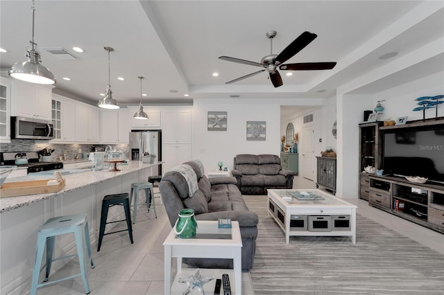 tiled living room featuring a raised ceiling and ceiling fan