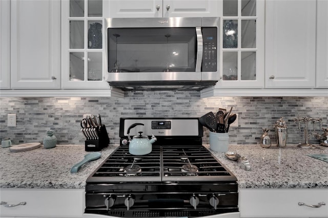 kitchen with light stone counters, range with gas cooktop, backsplash, and white cabinetry