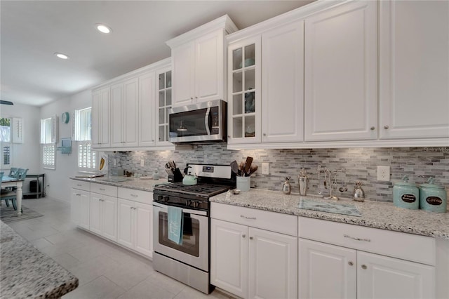 kitchen with white cabinets, backsplash, light stone counters, and appliances with stainless steel finishes