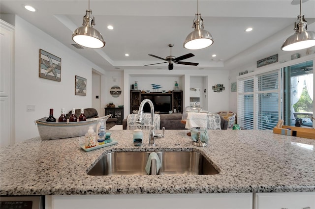 kitchen with a raised ceiling, light stone countertops, ceiling fan, pendant lighting, and sink