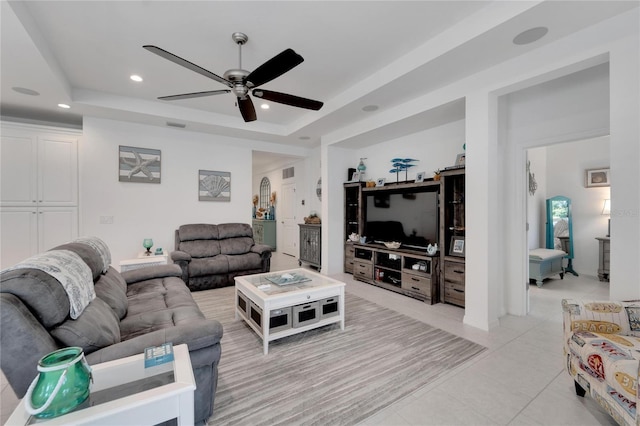 living room featuring ceiling fan, a raised ceiling, and light tile patterned floors