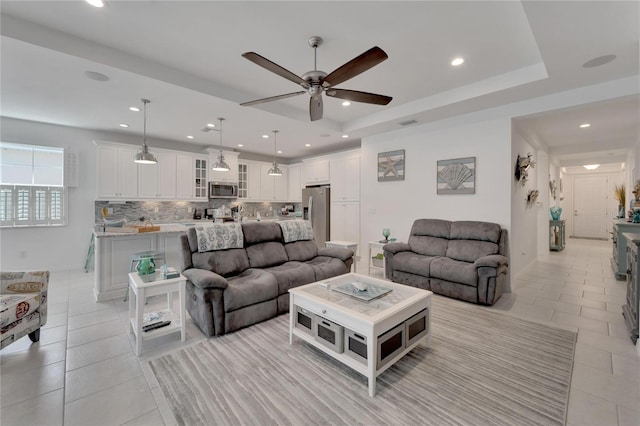 living room with ceiling fan, a raised ceiling, and light tile patterned flooring