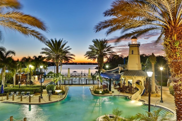 pool at dusk featuring a water slide and a water view