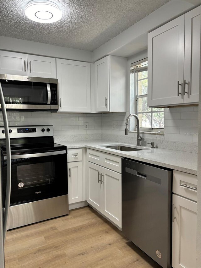 kitchen featuring sink, stainless steel appliances, light hardwood / wood-style flooring, and white cabinetry