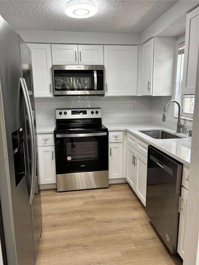 kitchen featuring appliances with stainless steel finishes, light hardwood / wood-style floors, sink, and white cabinetry