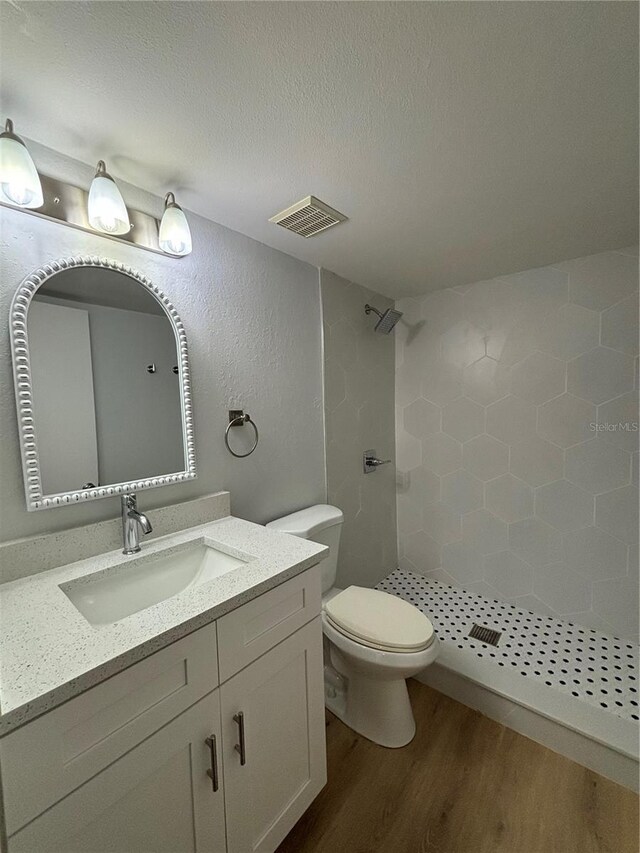 bathroom with a textured ceiling, a tile shower, wood-type flooring, vanity, and toilet