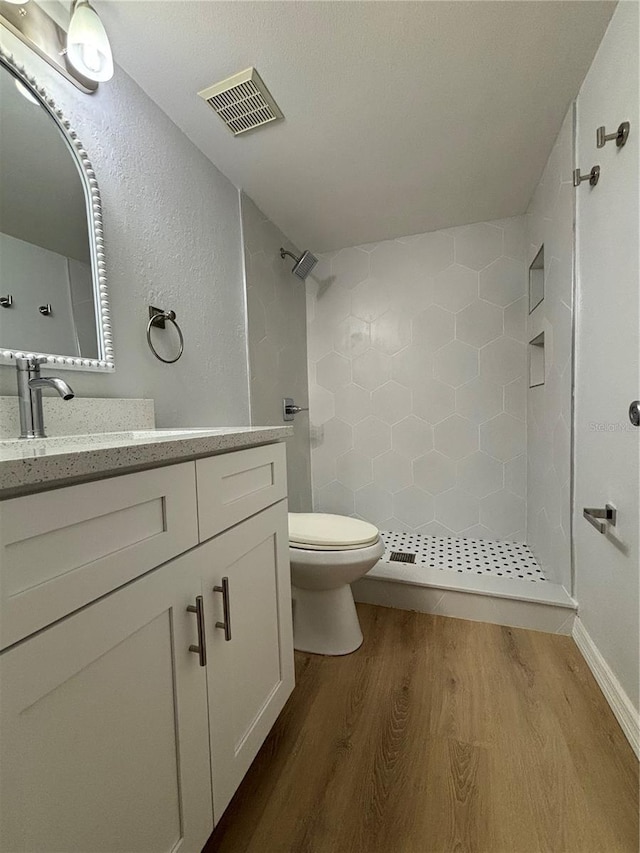 bathroom featuring wood-type flooring, a tile shower, toilet, and large vanity