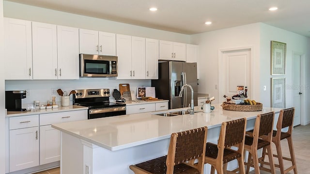 kitchen with white cabinets, a breakfast bar, an island with sink, and appliances with stainless steel finishes