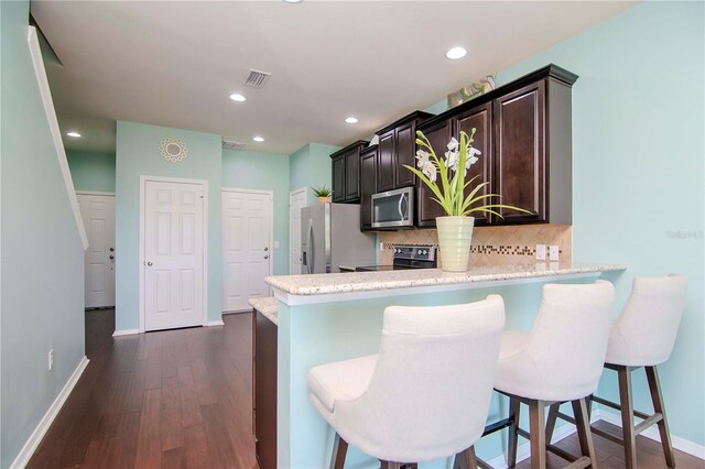 kitchen with decorative backsplash, appliances with stainless steel finishes, dark hardwood / wood-style flooring, kitchen peninsula, and a breakfast bar