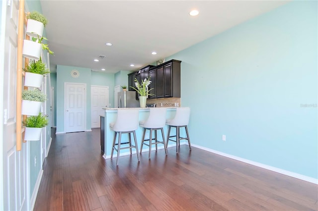 kitchen featuring a breakfast bar, stainless steel fridge, dark brown cabinetry, dark hardwood / wood-style flooring, and kitchen peninsula