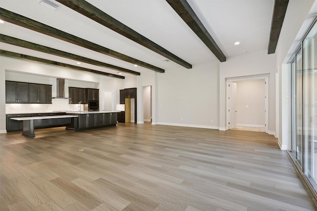 unfurnished living room featuring light hardwood / wood-style flooring, beamed ceiling, and sink