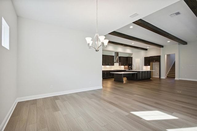 unfurnished living room with beamed ceiling, light wood-type flooring, an inviting chandelier, and sink