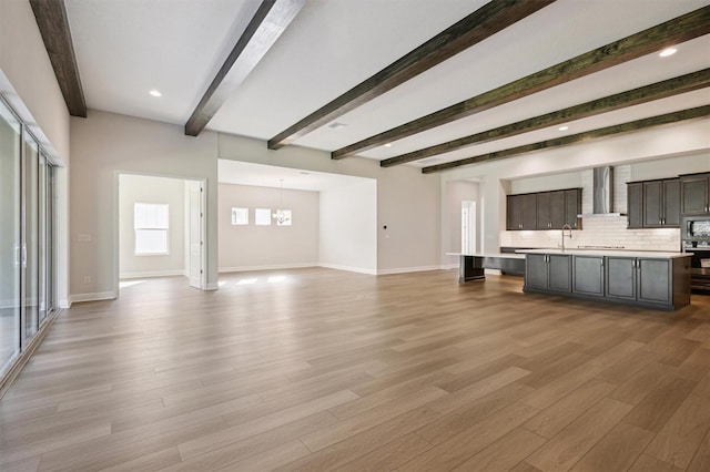 unfurnished living room with light hardwood / wood-style floors, sink, beam ceiling, and a chandelier