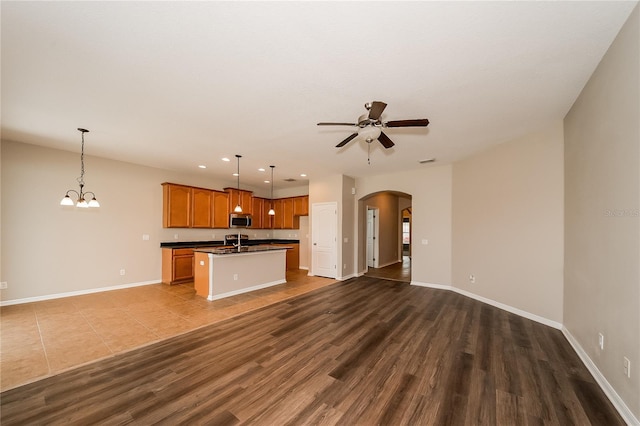 kitchen featuring sink, hanging light fixtures, dark hardwood / wood-style floors, an island with sink, and ceiling fan with notable chandelier