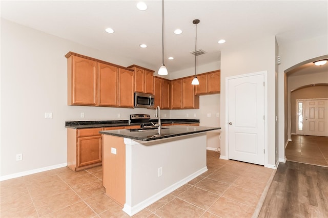 kitchen featuring a center island with sink, sink, dark stone countertops, decorative light fixtures, and stainless steel appliances