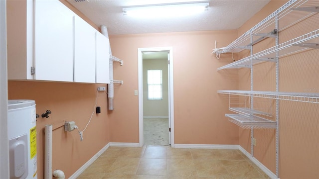 laundry room with light tile patterned flooring, cabinets, a textured ceiling, and water heater