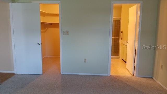 unfurnished bedroom featuring a closet, light colored carpet, a spacious closet, and ensuite bath