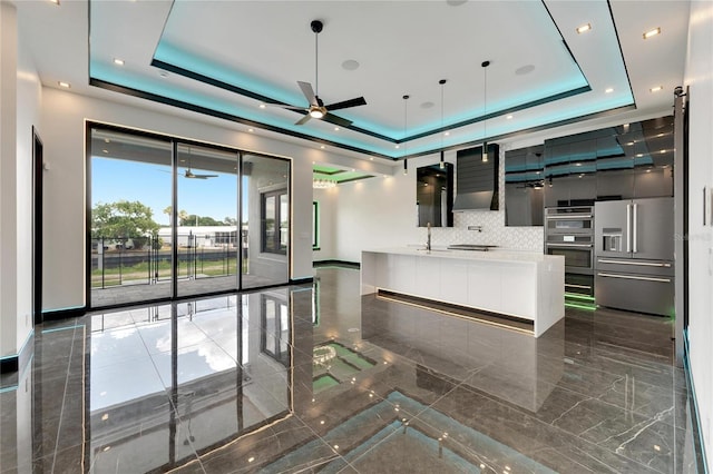 kitchen featuring a raised ceiling, ceiling fan, tasteful backsplash, decorative light fixtures, and stainless steel appliances