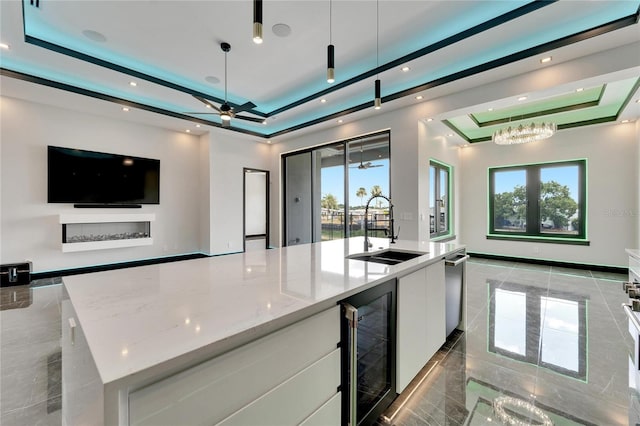 kitchen featuring white cabinetry, sink, wine cooler, a large island with sink, and a tray ceiling