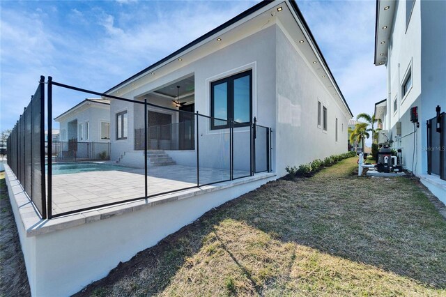 view of side of home featuring fence, a patio, a lawn, and stucco siding