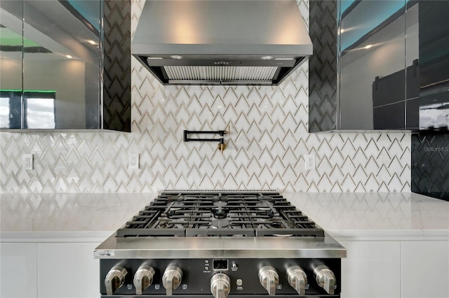 kitchen with cooktop, wall chimney range hood, light stone counters, and decorative backsplash