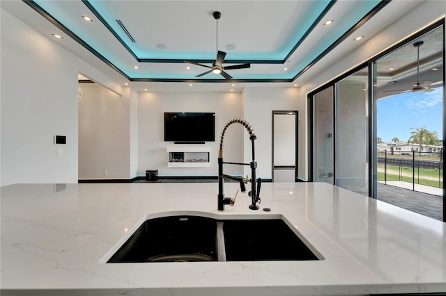 kitchen with a ceiling fan, open floor plan, a sink, and a raised ceiling