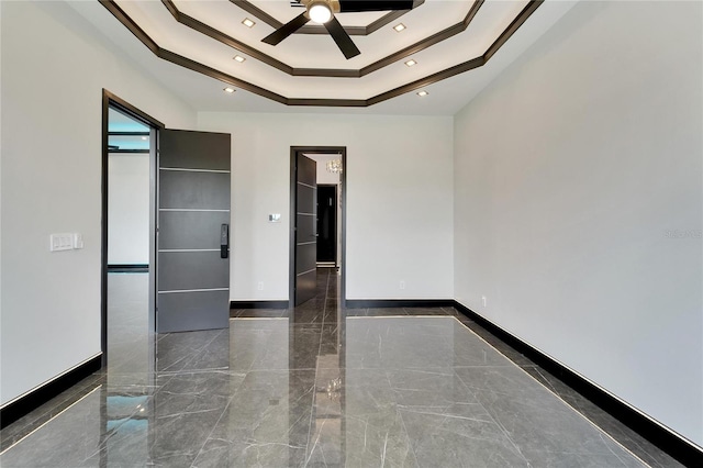 spare room featuring a ceiling fan, a tray ceiling, marble finish floor, and baseboards