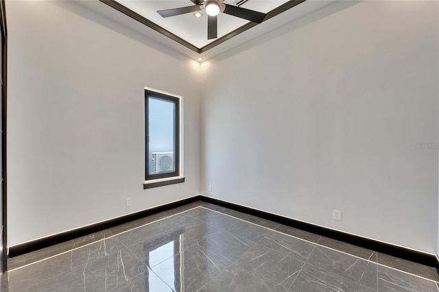 unfurnished room with a ceiling fan, marble finish floor, a raised ceiling, and baseboards