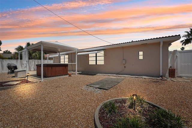 back house at dusk with a hot tub and a patio