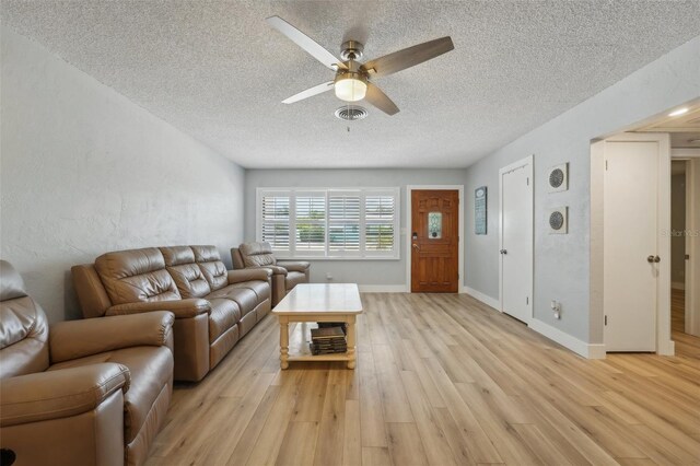 living room with a textured ceiling, ceiling fan, and light wood-type flooring