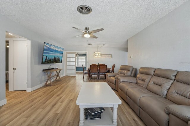 living room with a textured ceiling, ceiling fan, and light wood-type flooring