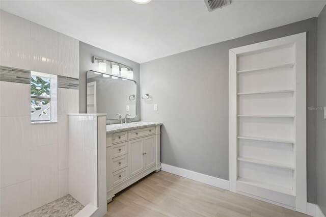 bathroom with a tile shower, built in features, wood-type flooring, and vanity