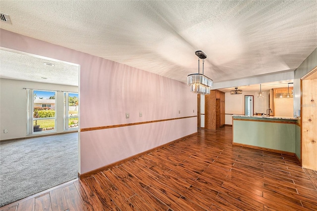 unfurnished living room featuring a textured ceiling, hardwood / wood-style flooring, a notable chandelier, and sink