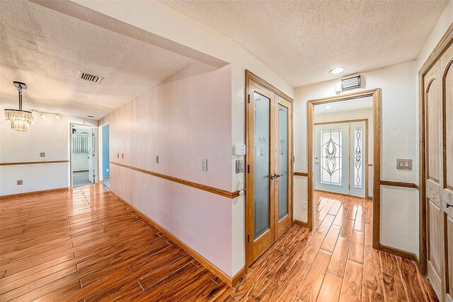 hall with hardwood / wood-style floors, a textured ceiling, and a chandelier