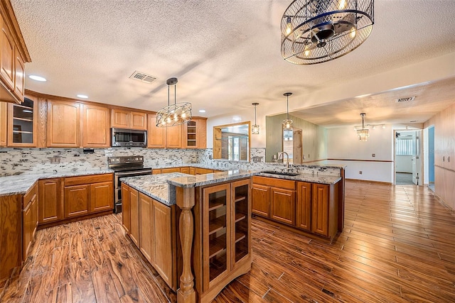 kitchen with kitchen peninsula, stainless steel appliances, sink, wood-type flooring, and a kitchen island