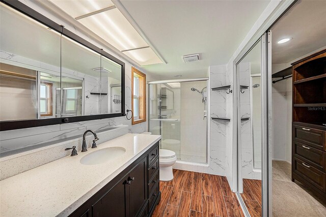 bathroom with hardwood / wood-style floors, vanity, toilet, and a shower with door