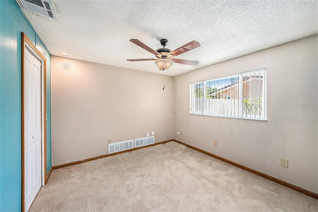 spare room with a textured ceiling, light colored carpet, and ceiling fan