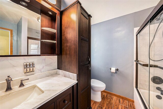 full bathroom with backsplash, bath / shower combo with glass door, vanity, hardwood / wood-style floors, and toilet