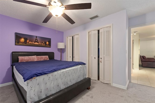 bedroom with multiple closets, ceiling fan, light colored carpet, and a textured ceiling