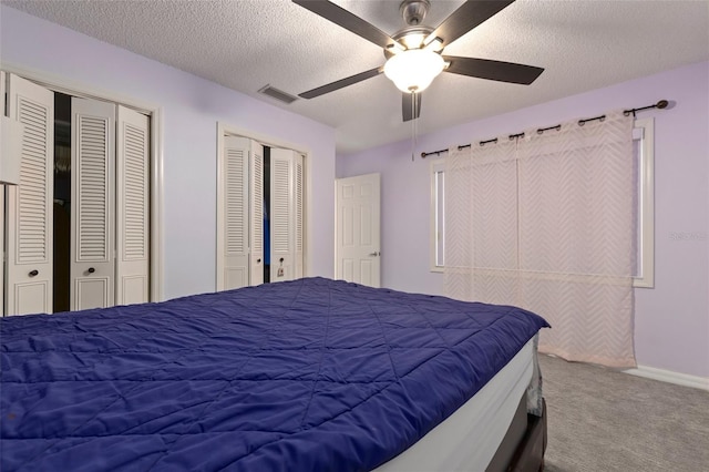 bedroom featuring carpet, a textured ceiling, ceiling fan, and multiple closets