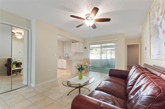 living room featuring ceiling fan, sink, light tile patterned flooring, and a textured ceiling