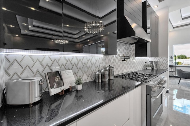 kitchen with white cabinetry, stainless steel range, wall chimney exhaust hood, decorative light fixtures, and a tray ceiling