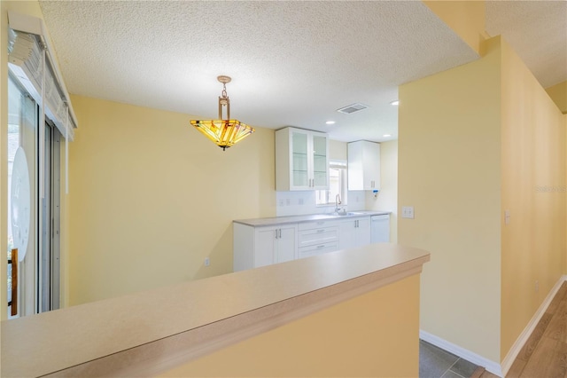 kitchen featuring decorative light fixtures, visible vents, white cabinetry, light countertops, and glass insert cabinets