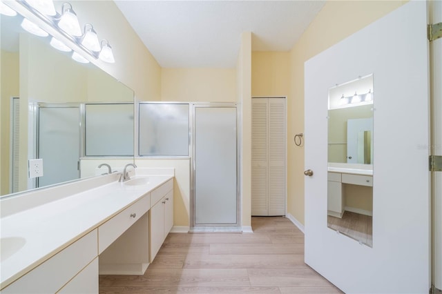 full bathroom with wood finished floors, a sink, a closet, a shower stall, and double vanity