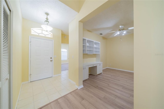 entrance foyer with light wood-style floors, built in study area, ceiling fan, a textured ceiling, and baseboards