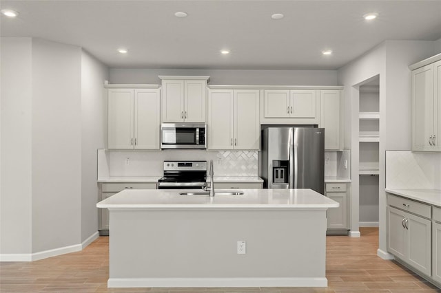 kitchen with appliances with stainless steel finishes, sink, light hardwood / wood-style flooring, and an island with sink