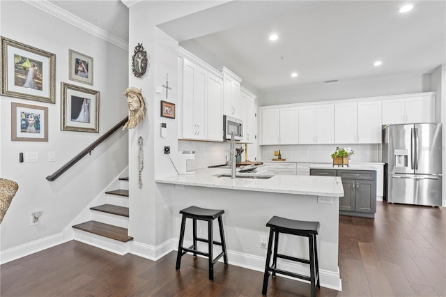 kitchen with a kitchen bar, kitchen peninsula, stainless steel appliances, dark wood-type flooring, and white cabinets