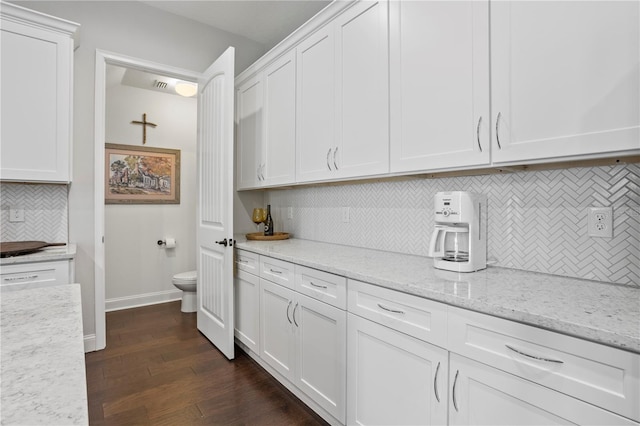 kitchen featuring white cabinets, dark hardwood / wood-style floors, light stone counters, and decorative backsplash